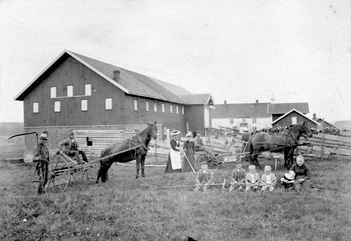 Folk på gården i høyonna, uthus, hovedbygning, hest, gjerde, låve, stabbur, våningshus, framhus, ljå, rake, fam. Rygg