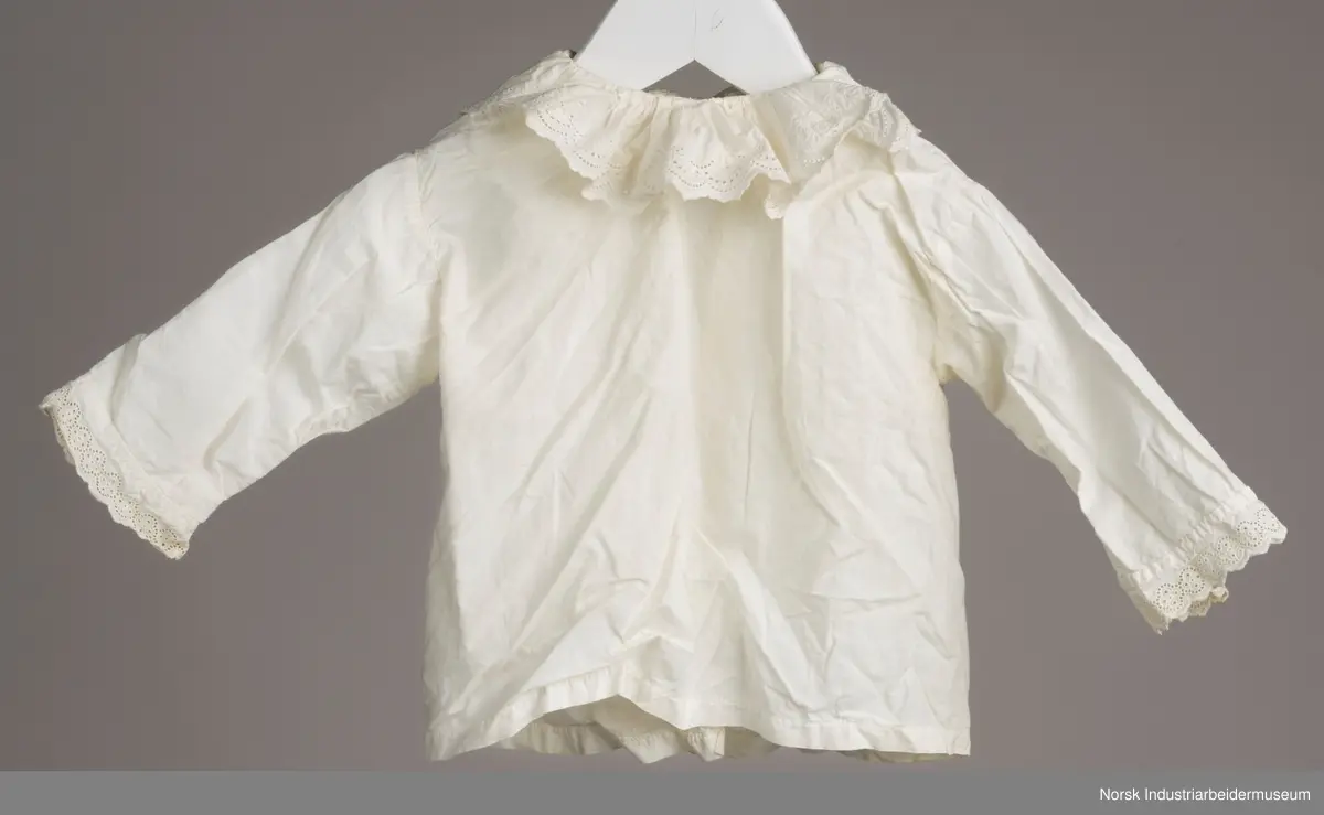 Hvit skjorte med snor i halsen. I kanten av kragen og i enden av ermene er det engelsk blonder.