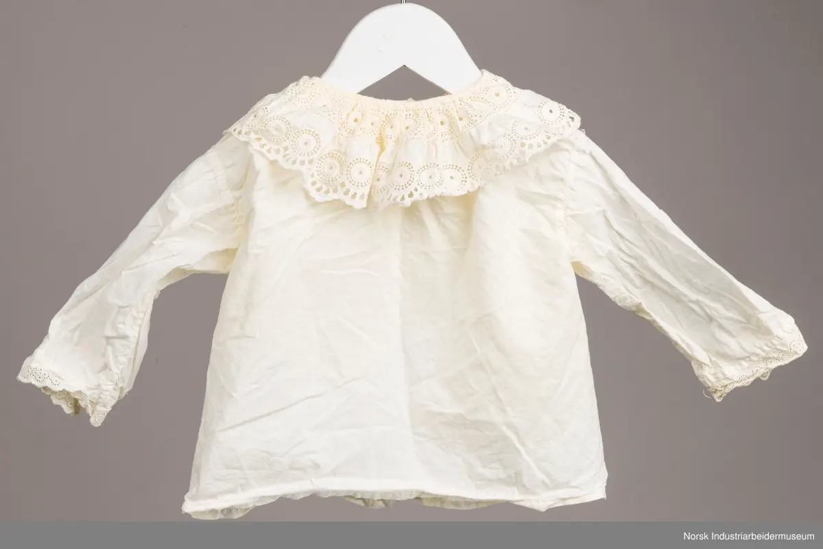 Hvit skjorte med snor i halsen. På kragen og i enden av ermene er det engelsk blonder. Kragen har to rader med blonder, en ytterst på kragen og en mot halsen.