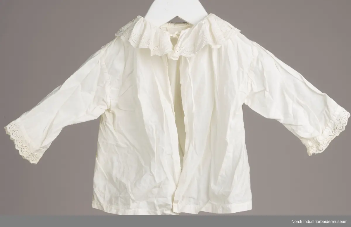 Hvit skjorte med snor i halsen. I kanten av kragen og i enden av ermene er det engelsk blonder.