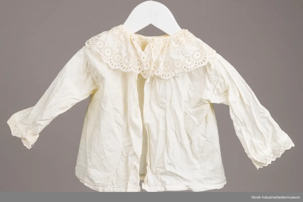 Hvit skjorte med snor i halsen. På kragen og i enden av ermene er det engelsk blonder. Kragen har to rader med blonder, en ytterst på kragen og en mot halsen.