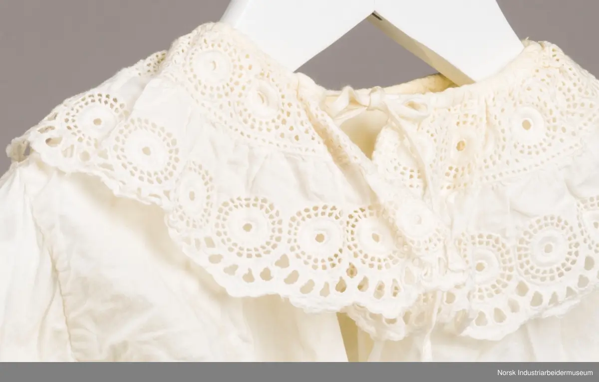 Hvit skjorte med snor i halsen. På kragen og i enden av ermene er det engelsk blonder. Kragen har to rader med blonder, en ytterst på kragen og en mot halsen.