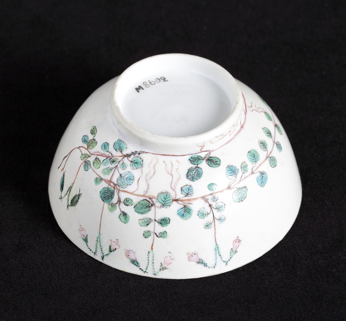 Tekopp av porslin. Dekor med blommande linnéor i rosa och gröna nyanser runt om.
Tillhörande tefat finns.

Inskrivet i huvudkatalog 1935.