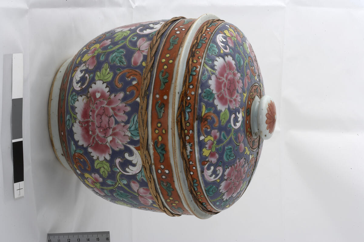 Bencharong.Jar with cover. Peony and flower design on blue background. Red band around the base, rim, cover rim and knob, with stylized floral design (diamonds, dots, leaves). Undecorated footring. Domed cover with outturned rim with brown iron oxide embedded in the glaze, flat knob with a red flower. Rotting band around the jar. Jar diameter 20.8 cm, height 15.5 cm. Late 18th -19th century.   