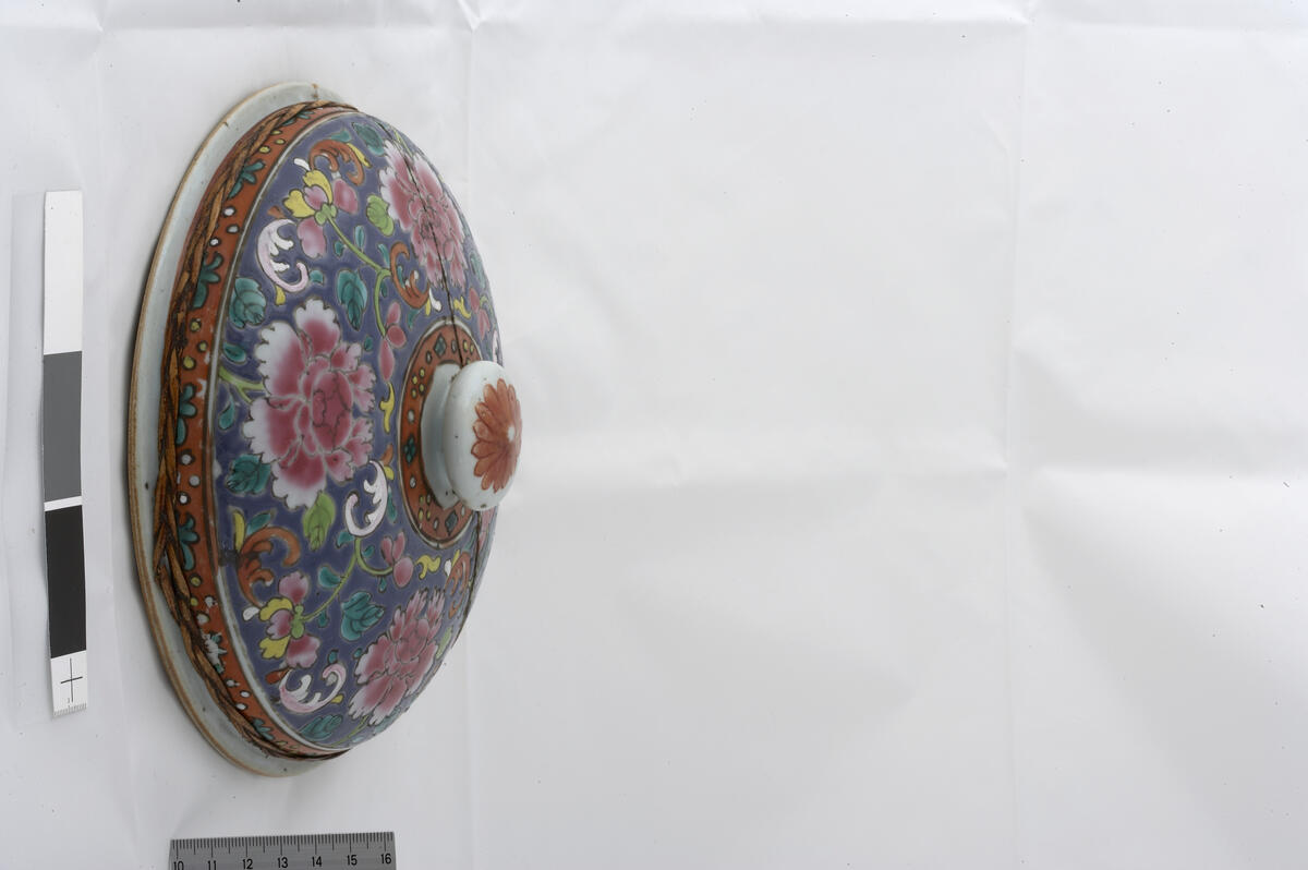 Bencharong.Jar with cover. Peony and flower design on blue background. Red band around the base, rim, cover rim and knob, with stylized floral design (diamonds, dots, leaves). Undecorated footring. Domed cover with outturned rim with brown iron oxide embedded in the glaze, flat knob with a red flower. Rotting band around the jar. Cover diameter 21 cm, height 7 cm. Late 18th -19th century.