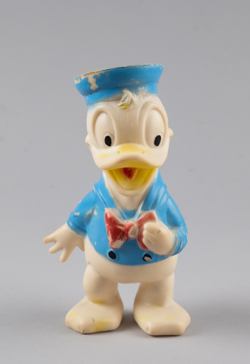 Leketøy av mykplast i form av en Donald Duck. Den er hvit med blå jakke med svarte knapper og rød sløyfe, den har blå hatt og gult nebb med rød tunge.