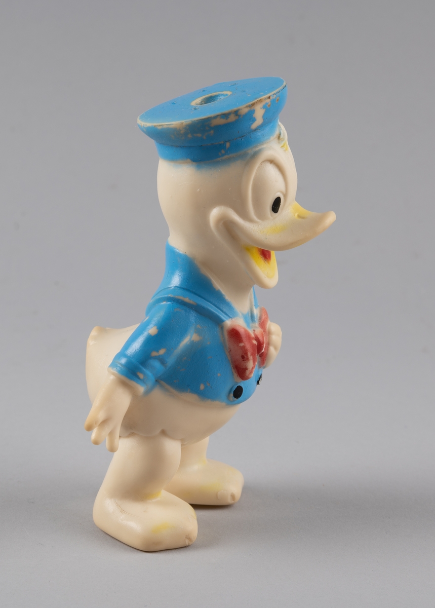 Leketøy av mykplast i form av en Donald Duck. Den er hvit med blå jakke med svarte knapper og rød sløyfe, den har blå hatt og gult nebb med rød tunge.