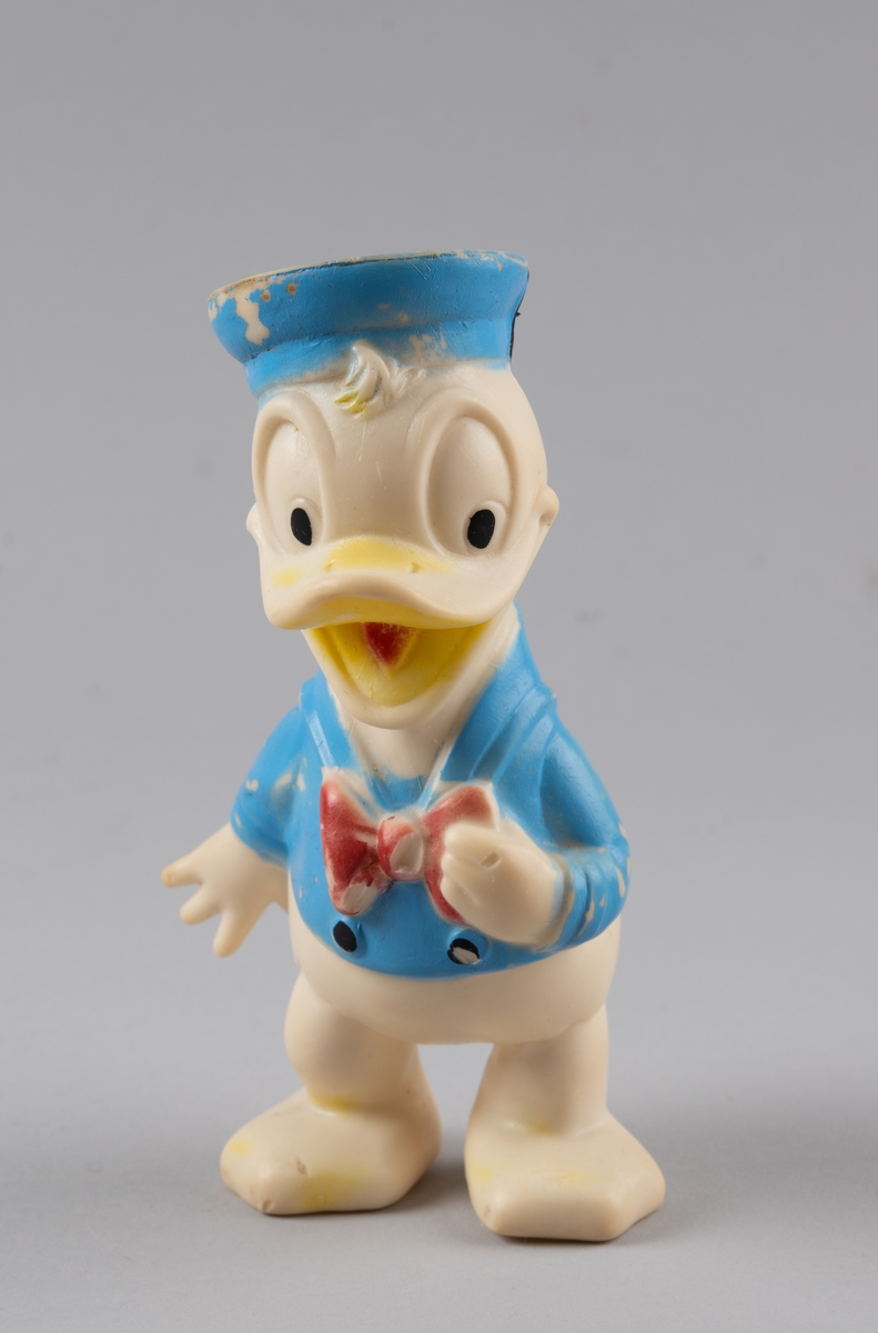 Leketøy av mykplast i form av en Donald Duck. Den er hvit med blå jakke med svarte knapper og rød sløyfe, den har blå hatt og gult nebb med rød tunge.