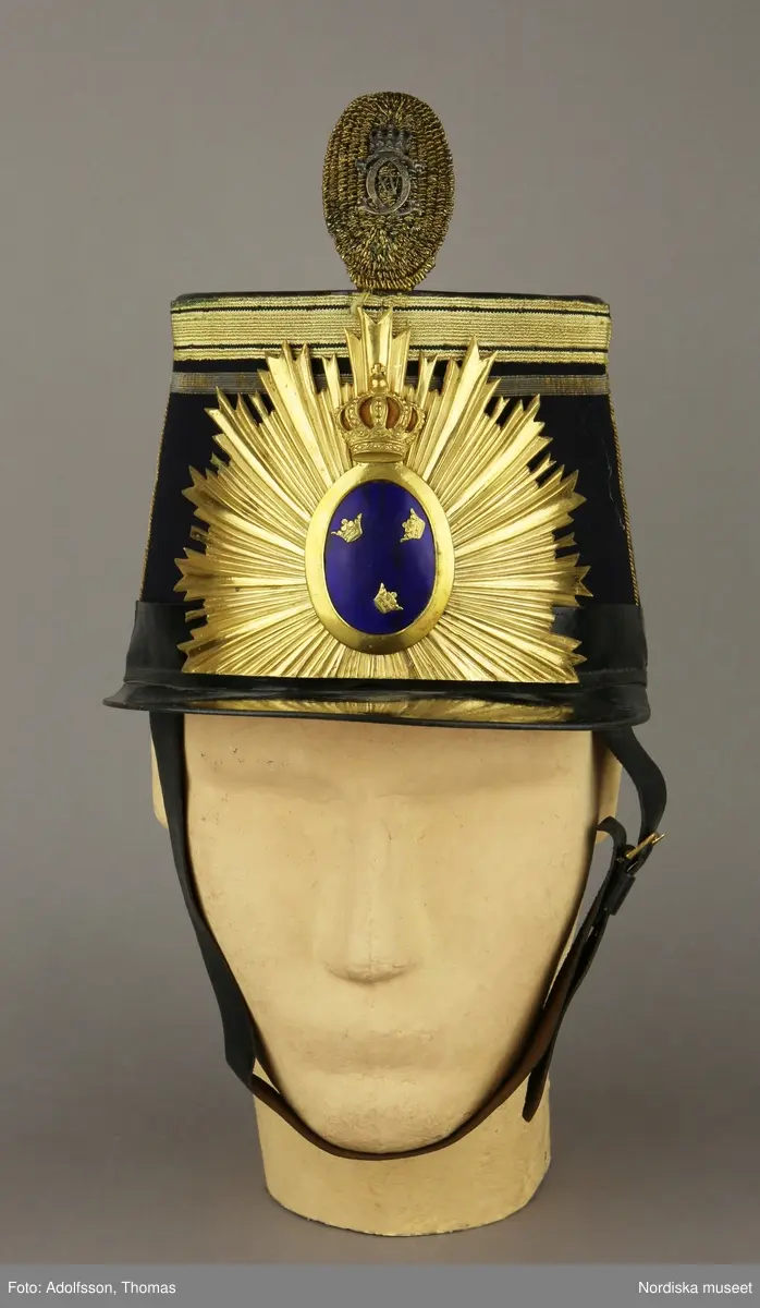 Huvudliggaren:
"Hatt, Kepi m.m.
Tillhört Stockholms borgerskaps infanteri-uniform.
a) Trekantig hatt med plym.
b) Kepi. Märkt: [avtecknat C i dubbelmonogram och XV] med plym.
c) Epåletter märkta: FYRWALD".
d) Huggvärja. Fäste af mässing, med bygel, parerstång och parerplåt, skaften lindad med silfvertråd, knappen urnformig, upptill med platta, för sigill; klingan eneggad och prydd med vapentrofeer m.m. i etsning.
e) 24 knappar.
G. af skomakaren C. A. Hedman i Stockholm. 29/5 1883."