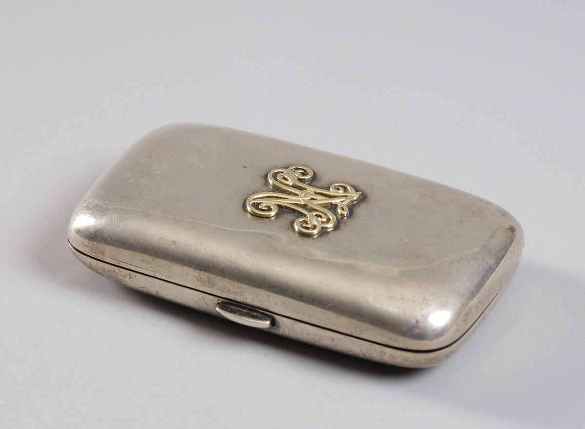 Cigarettetui i silver med monogram K.N. i förgylld relief på ena sidan. Andra sidan graverad graverad "Souvenir de Christine Nilsson" etuiet inuti förgyllt med rikt ornerade klämmor.

Inskrivet i huvudkatalog 1933.