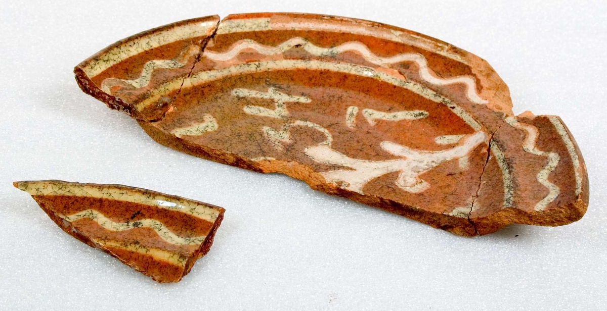 Kärl, delar av kärl. Keramik, lergods.
1) Fat med vitlerdekor. Målat årtal ...34.
2) En kruka med kärnor från körsbär och plommon.
3) Två fat.