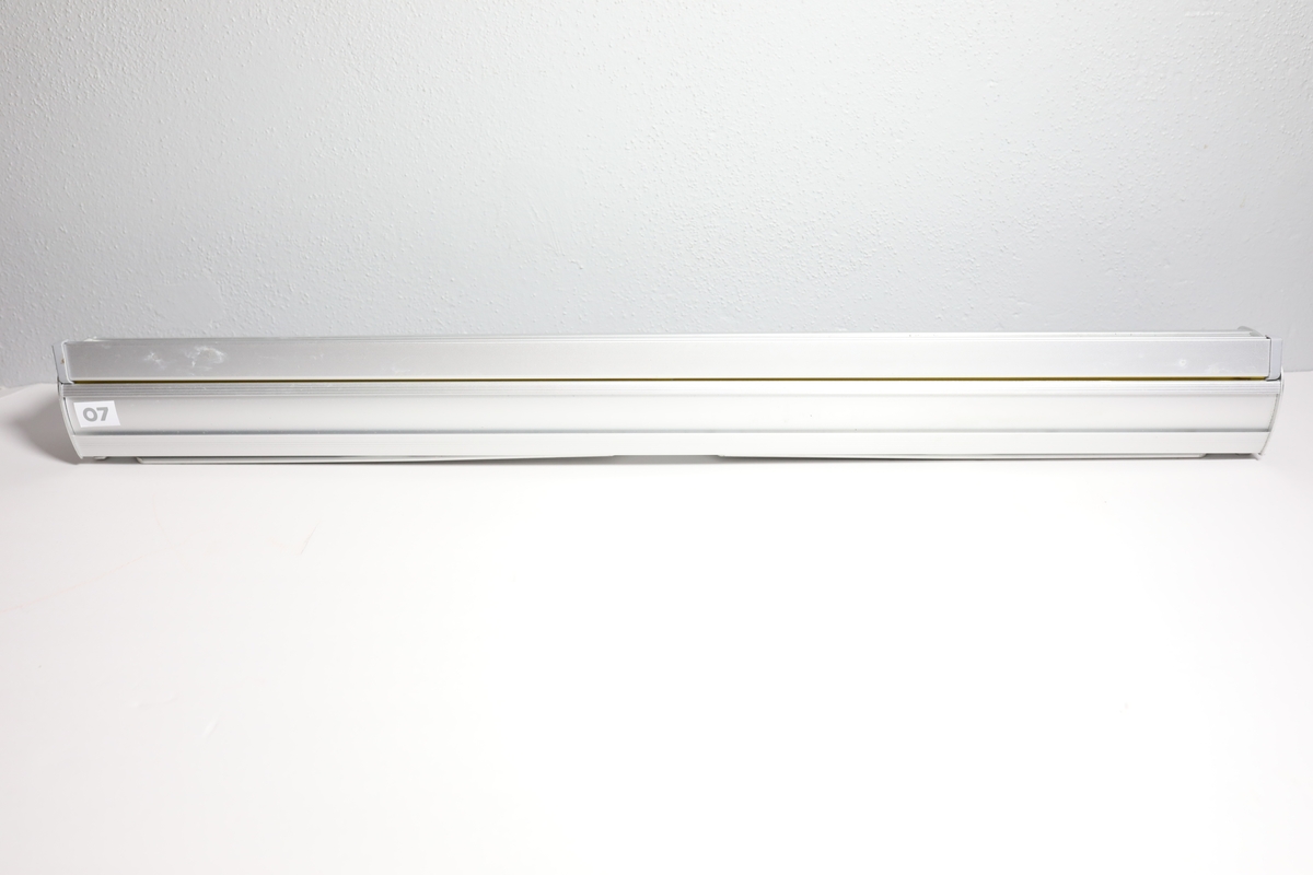 Rollup med med etui, har en stang bak til å holde den oppe. Den har informasjon på engelsk om å bruke maske og holde en meter avstand for å stoppe covid-19. Enkelt bilde av kvinnehodet med ansiktsmaske i mellom tittelen og informasjonen. I bunnen logo til Helsedirektoratet og FHI. Det er teipet over noe tekst i mellom informasjonen og logoene.