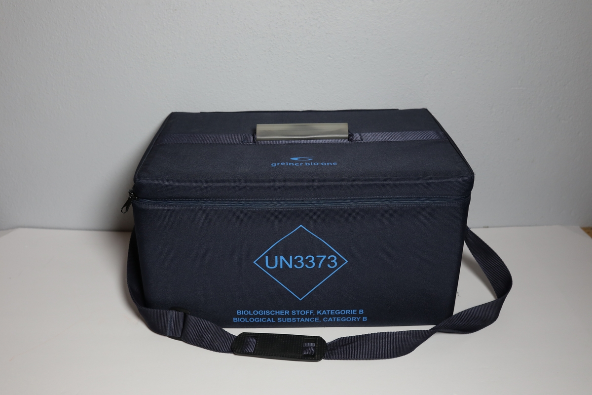 Bag med rom til tre bokser "Vacuette Transport Box" som det ble fraktet Covid-tester i. Glidlås rundt toppen av bagen. Den har håntak i midten av toppen, og på kortside er det feste for strop som man kan bære bagen med. På baksiden er det plastlomme med informasjon. Boksene har gjennomsiktige lokk, og har skumformer i til å plassere opp til 40 testrør i.