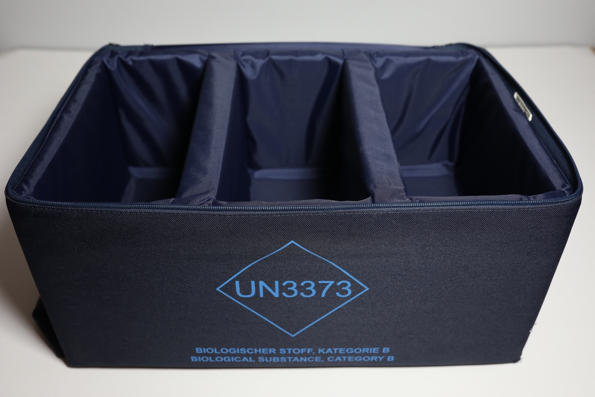 Bag med rom til tre bokser "Vacuette Transport Box" som det ble fraktet Covid-tester i. Glidlås rundt toppen av bagen. Den har håntak i midten av toppen, og på kortside er det feste for strop som man kan bære bagen med. På baksiden er det plastlomme med informasjon. Boksene har gjennomsiktige lokk, og har skumformer i til å plassere opp til 40 testrør i.