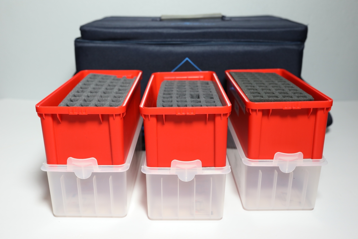 Bag med rom til tre bokser "Vacuette Transport Box" som det ble fraktet Covid-tester i. Glidlås rundt toppen av bagen. Den har håntak i midten av toppen, og på kortside er det feste for strop som man kan bære bagen med. På baksiden er det plastlomme med informasjon. Boksene har gjennomsiktige lokk, og har skumformer i til å plassere opp til 40 testrør i.