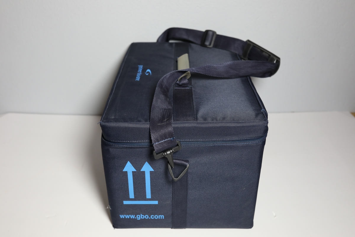 Bag med rom til tre bokser "Vacuette Transport Box" som det ble fraktet Covid-tester i. Glidlås rundt toppen av bagen. Den har håntak i midten av toppen, og på kortside er det feste for strop som man kan bære bagen med. På baksiden er det plastlomme med informasjon. Boksene har gjennomsiktige lokk, og har skumformer i til å plassere opp til 40 testrør i.
