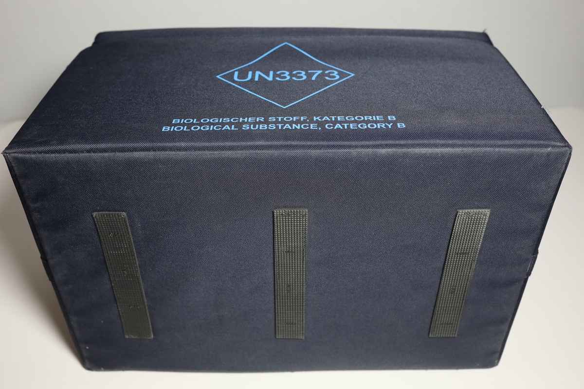 Bag med rom til tre bokser "Vacuette Transport Box" som det ble fraktet Covid-tester i. Glidlås rundt toppen av bagen. Den har håntak i midten av toppen, og på kortside er det feste for strop som man kan bære bagen med. På baksiden er det plastlomme med informasjon. Boksene har gjennomsiktige lokk, og har skumformer i til å plassere opp til 40 testrør i.