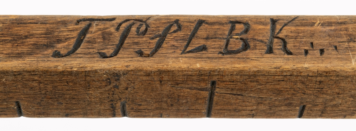 Målestav laget av tremateriala, antakelig bjørkevirke. Gjenstanden er 73,6 centimeter lang og har et rektangulært tverrsnitt, som er noe smalere i den fremre enn i den bakerste enden. Aller bakerst er det et cirka 10,5 centimeter langt handtak med et dråpeformet gjennombrutt hull, antakelig for oppheng. Den rektangulære delen har inskårne streker, som markerer lengdemål i alen, fot, tommer og halvtommer, etter det som var gjeldende standard i Norge fra 1824 til 1875. 1824-standarden var for øvrig bare en forsiktig justering av en tidligere standard fra 1683. Omregnet i metriske enheter, som har vært standarden i de fleste sammenhenger her til lands siden, skulle en alen være 62,75 centimeter. Dette er det lengste målet denne målestaven har. En alen kunne deles i 2 fot, 24 tommer og 48 halvtommer, noe som altså er gjort på denne målestaven. Gjestanden har et innskåret årstall - «1853», som kan ha vært produksjonsåret - og bokstavkonstellasjonen «TPSLBK», som antakelig refererer til Tollev Pedersen Lillebekken (1822-1902) fra Tolga i Nord-Østerdalen.