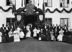 Ståndsmässigt bröllop på Karlshov i Älvestad. I den lövade porten står dagens huvudpersoner kamrer Fredrik Rosin och Ingrid Fredholm. Till höger om sig har bruden sin far August Fredholm, ägare av godset. Övriga personer som identifierats i bilden är godsägare Fredholms andra hustru Helga (med sin hatt över sina knän) och makarnas minderåriga barn Signe, Jane, Hildur och Einar. Övriga personer i bilden är oss okända. Dock påvisar den stående mannen längts till vänster i gruppen män till höger stora likheter med godsägare Melker Falkenberg till Brokind. Mannen längst till höger i samma grupp påminner väl om entreprenören Jonn O Nilson.