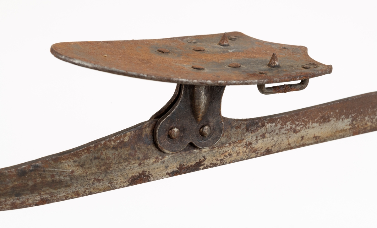 Skøyter av stål, av en modell som skulle bindes fast under sålene på sko som ellers ble brukt på andre underlag enn skøyteis. Skøytene er 36,5 centimeter lange. De delene av stålene eller skjærene som skulle sli på isen er planslipte og om lag 5 millimeter brede (en aning bredere bak enn foran) og har oppovervendte «snabler» i de fremre endene. De oppovervendte delene av de samme stålene er noe smalere. På disse er det påklinket beslag som bærer stålplater, ei som skulle tjene som underlag for ballepartiet på skosålen og ei for hælen. Hælplatene har to oppovervendte «ører» som skulle forebygge at skosålene skled bakover. På undersidene av de nevnte stålplatene er det kramper som tjente som smøyestoler for reimene som ble brukt når skøytene skulle spennes fast på skoene. På oversidene av hælplatene er det en oppovervendt pigg, på «tåballeplatene» er det to slike pigger. Disse skulle trenge inn i skosålene og forebygge at skøytene forskjøv seg sidevegs. Skøytene er masseproduserte, stemplet «32», men har ingen stempler som navngir produsenten. Metallet er noe rustent.