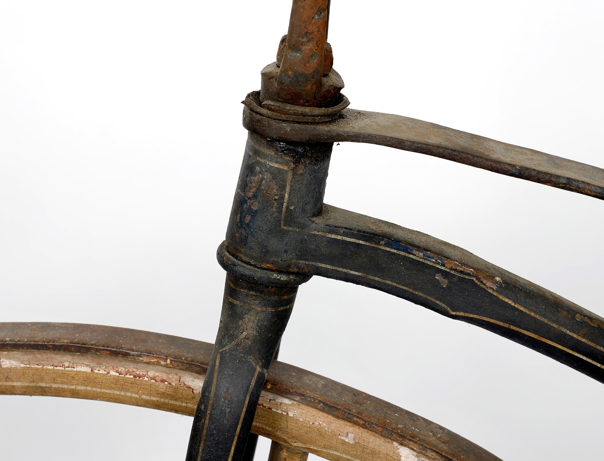 Sykkel av jern med hjul i tre med jernbånd/skoning ytterst. Hjulene har ulik størrelse, størst foran, kan ha vært kjerrehjul en gang, men er laget i smekre materialer. Bemalt i beige med kremhvite linjer, mulig rødt under? Jernrammen er svart, med rester etter dekorasjon i form av linjer. Pedaler på framhjulet (samme system som velte-petter). Trehåndtak. Setet har små huller ytterst som kan ha vært feste for polstring/lær.