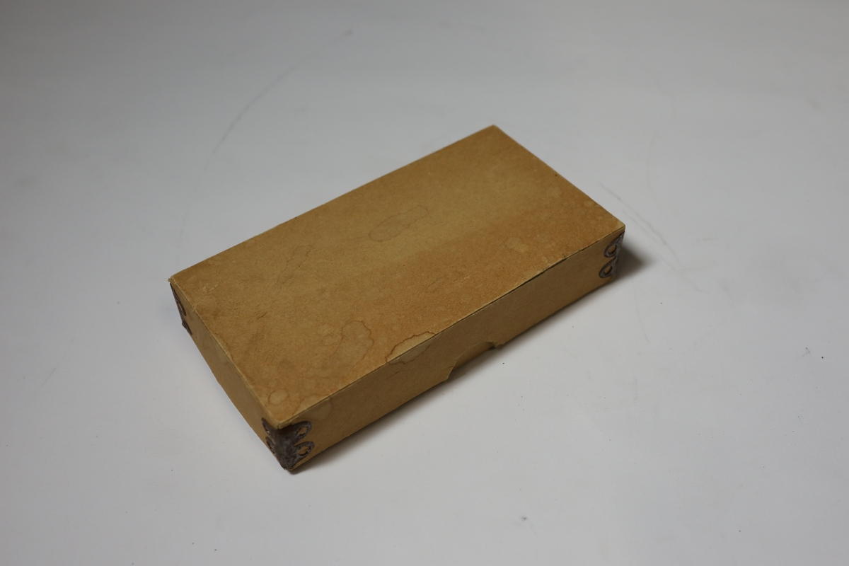 Sjakkbrett i eske med lokk. Rundt kanten er det bokstaver og tall for rutene, og rutene har hull i midten som brikkene kan festes i. Brettet er delt i to og hengslet på midten under. Det er hullrom under med bunn dekket med stoff der brikkene kan oppbevares når brettet er lukket sammen.