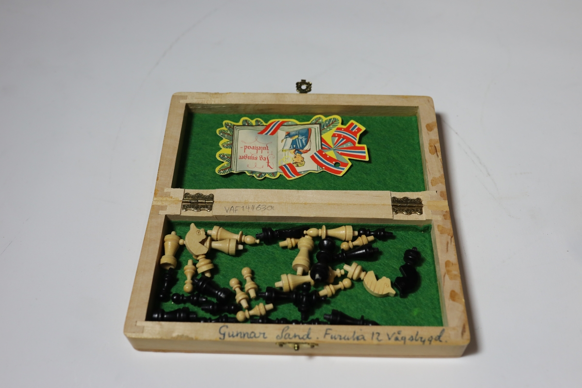 Sjakkbrett i eske med lokk. Rundt kanten er det bokstaver og tall for rutene, og rutene har hull i midten som brikkene kan festes i. Brettet er delt i to og hengslet på midten under. Det er hullrom under med bunn dekket med stoff der brikkene kan oppbevares når brettet er lukket sammen.