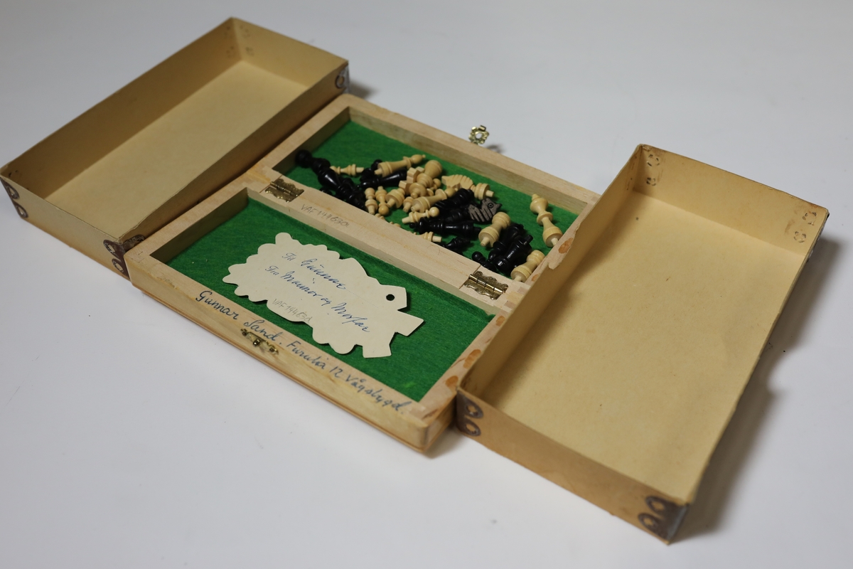 Sjakkbrett i eske med lokk. Rundt kanten er det bokstaver og tall for rutene, og rutene har hull i midten som brikkene kan festes i. Brettet er delt i to og hengslet på midten under. Det er hullrom under med bunn dekket med stoff der brikkene kan oppbevares når brettet er lukket sammen.