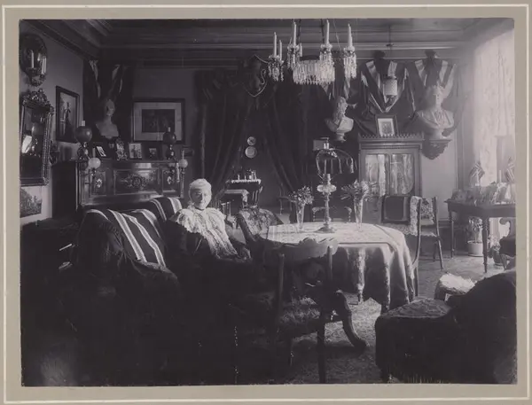 Maren Sars hjemme i salongen på Frogner. Vi finner nasjonale symboler i interiøret: Norske flagg på bordet, bysten av Bjørnstjerne Bjørnson oppe på veggen og portrettene av svigersønnen på pianoet.