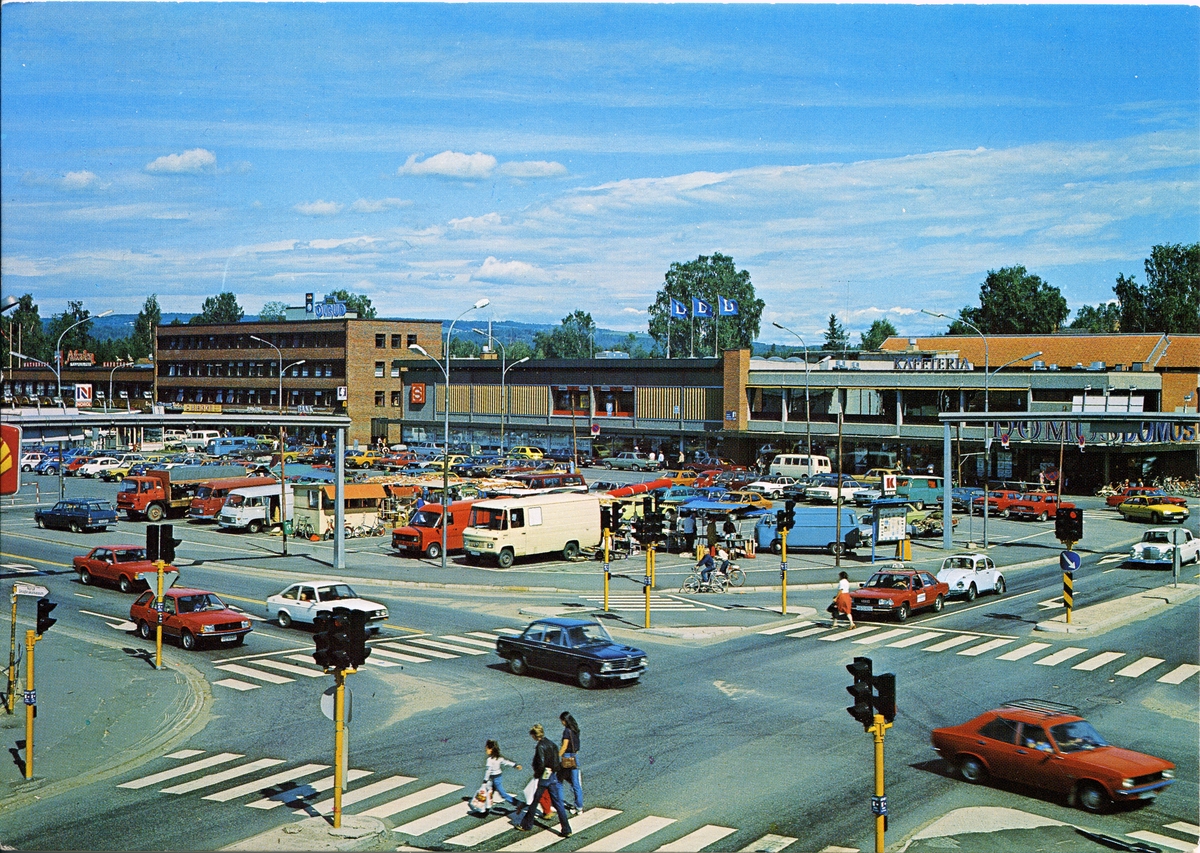 Torget / Torvet.Postkort.
Arkaden, Domus, Kafeteria, Rutebilstasjon.Lyskryss.
Parkeringsplass med mange biler.