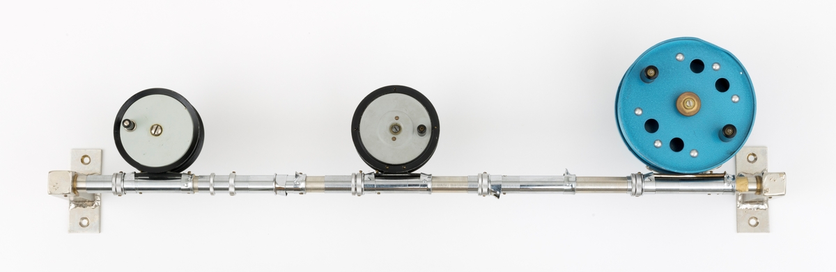 Tre fiskesneller, to fluesneller og en dorge- pilkesnelle, montert på et rør (en stang) med fem snellfester. I og med at det er fem snellefester kan det tyde på at det en gang har vært montert fem sneller på stanga. Snellene er produsert av firmaet Asbjørn Hørgård A/S i Trondheim. I hver ende av røret er det montert fester som gjør det mulig å montere stanga med fiskesneller til vegg. Snellene sitter festet på undersiden av stanga når de brukes, altså med snellefoten opp. 

I salgskatalogen "Råd og redskap fra Hørgård" i 1984 er den blå dorge- pilksnella  beskrevet slik: "Napptun snelle 51/2' * K(EK) Enklere kan en snelle knapt bli. Du kan enten bruke den som pilkesnelle eller du kan dorge med den på sjøen eller etter større innlandsfisk. Snelle har klikk som gir deg et signal når fisken går på. Klikken slår du på ved å skyve på knotten bak. Den store trommelen gjør at det er lett å ta inn fisk. På kanten av spolen har du en bremseflate, som du legger håndflaten på når fiske renner ut. Kan anbefales sammen Frøya. Pris: Napptun m/klikk kr. 205."
Diameter sidedeksel: 14 cm. Bredde målt frfa ytterside av sveivknapper til ytterside av sidedeksel: 8, 2 cm. 

Fluesnellene: Snellene består av spole (trommel), sidedeksler, ramme, sveiv og snellefot. Sveiva er montert direkte på spolen. 
På svart og hvit fluesnelle som er merket Trout Fly sitter sveivknappen løst. Snella merket Trout Fly har disse målene: 
Bredde målt fra ytterside av sveivknapp til ytterside av sidedeksel: 5,6 cm. Bredde spole, innvendig målt: 2,4 cm Diameter sidededeksel: 9,1 cm.
I Hørgård-firmaets bok "Norwegian made fishing tackle" fra 1964 er denne snelletypen beskrevet slik: "Trout Fly 3 1/2" Guttsnelle, passende for flue-, mark- og dorgefiske."

På svart og hvit fluesenlle som er merket Å H Hørgård er disse målene tatt: 
Bredde målt fra ytterside av sveivknapp til ytterside av sidedeksel: 6,4 cm. Bredde spole, innvendig målt: 2,2 cm Diameter sidededeksel: 8,9 cm.
I Hørgård-firmaets bok "Norwegian made fishing tackle" fra 1964 er denne snelletypen beskrevet slik: "Ørret fluesnelle 3 1/2'' ca. 170 gr. Presjonsarbeid med utsøkt materiale. Helstøpt lettmetall. Brennlakkert. Kapasitet: 30 yds. tapered fluesnøre og ca. 50 yds. bakline."



[Se fanen Opplysninger for informasjon om Asbjørn Hørgård og hans firma.]