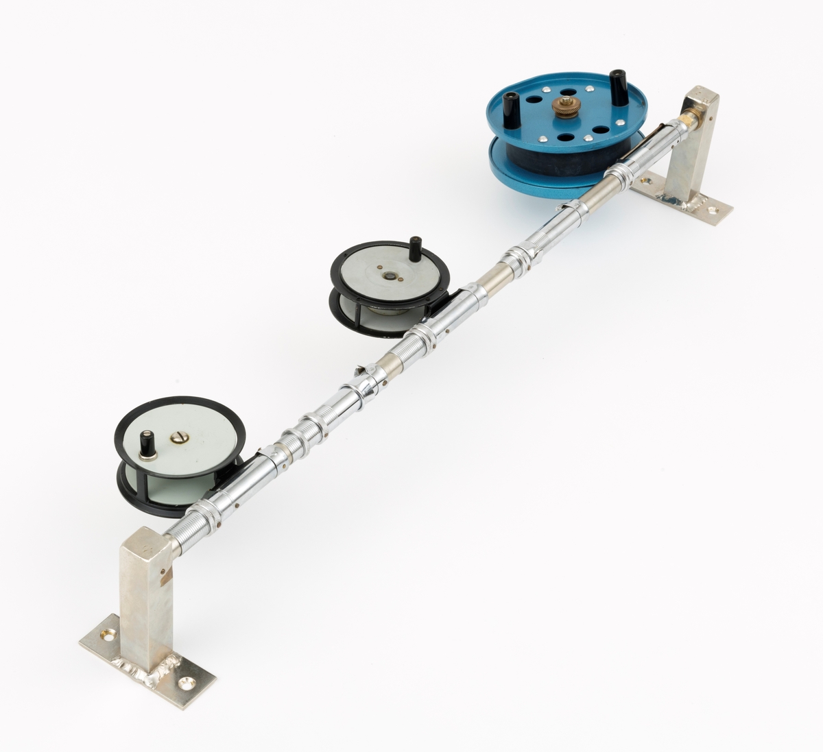 Tre fiskesneller, to fluesneller og en dorge- pilkesnelle, montert på et rør (en stang) med fem snellfester. I og med at det er fem snellefester kan det tyde på at det en gang har vært montert fem sneller på stanga. Snellene er produsert av firmaet Asbjørn Hørgård A/S i Trondheim. I hver ende av røret er det montert fester som gjør det mulig å montere stanga med fiskesneller til vegg. Snellene sitter festet på undersiden av stanga når de brukes, altså med snellefoten opp. 

I salgskatalogen "Råd og redskap fra Hørgård" i 1984 er den blå dorge- pilksnella  beskrevet slik: "Napptun snelle 51/2' * K(EK) Enklere kan en snelle knapt bli. Du kan enten bruke den som pilkesnelle eller du kan dorge med den på sjøen eller etter større innlandsfisk. Snelle har klikk som gir deg et signal når fisken går på. Klikken slår du på ved å skyve på knotten bak. Den store trommelen gjør at det er lett å ta inn fisk. På kanten av spolen har du en bremseflate, som du legger håndflaten på når fiske renner ut. Kan anbefales sammen Frøya. Pris: Napptun m/klikk kr. 205."
Diameter sidedeksel: 14 cm. Bredde målt frfa ytterside av sveivknapper til ytterside av sidedeksel: 8, 2 cm. 

Fluesnellene: Snellene består av spole (trommel), sidedeksler, ramme, sveiv og snellefot. Sveiva er montert direkte på spolen. 
På svart og hvit fluesnelle som er merket Trout Fly sitter sveivknappen løst. Snella merket Trout Fly har disse målene: 
Bredde målt fra ytterside av sveivknapp til ytterside av sidedeksel: 5,6 cm. Bredde spole, innvendig målt: 2,4 cm Diameter sidededeksel: 9,1 cm.
I Hørgård-firmaets bok "Norwegian made fishing tackle" fra 1964 er denne snelletypen beskrevet slik: "Trout Fly 3 1/2" Guttsnelle, passende for flue-, mark- og dorgefiske."

På svart og hvit fluesenlle som er merket Å H Hørgård er disse målene tatt: 
Bredde målt fra ytterside av sveivknapp til ytterside av sidedeksel: 6,4 cm. Bredde spole, innvendig målt: 2,2 cm Diameter sidededeksel: 8,9 cm.
I Hørgård-firmaets bok "Norwegian made fishing tackle" fra 1964 er denne snelletypen beskrevet slik: "Ørret fluesnelle 3 1/2'' ca. 170 gr. Presjonsarbeid med utsøkt materiale. Helstøpt lettmetall. Brennlakkert. Kapasitet: 30 yds. tapered fluesnøre og ca. 50 yds. bakline."



[Se fanen Opplysninger for informasjon om Asbjørn Hørgård og hans firma.]