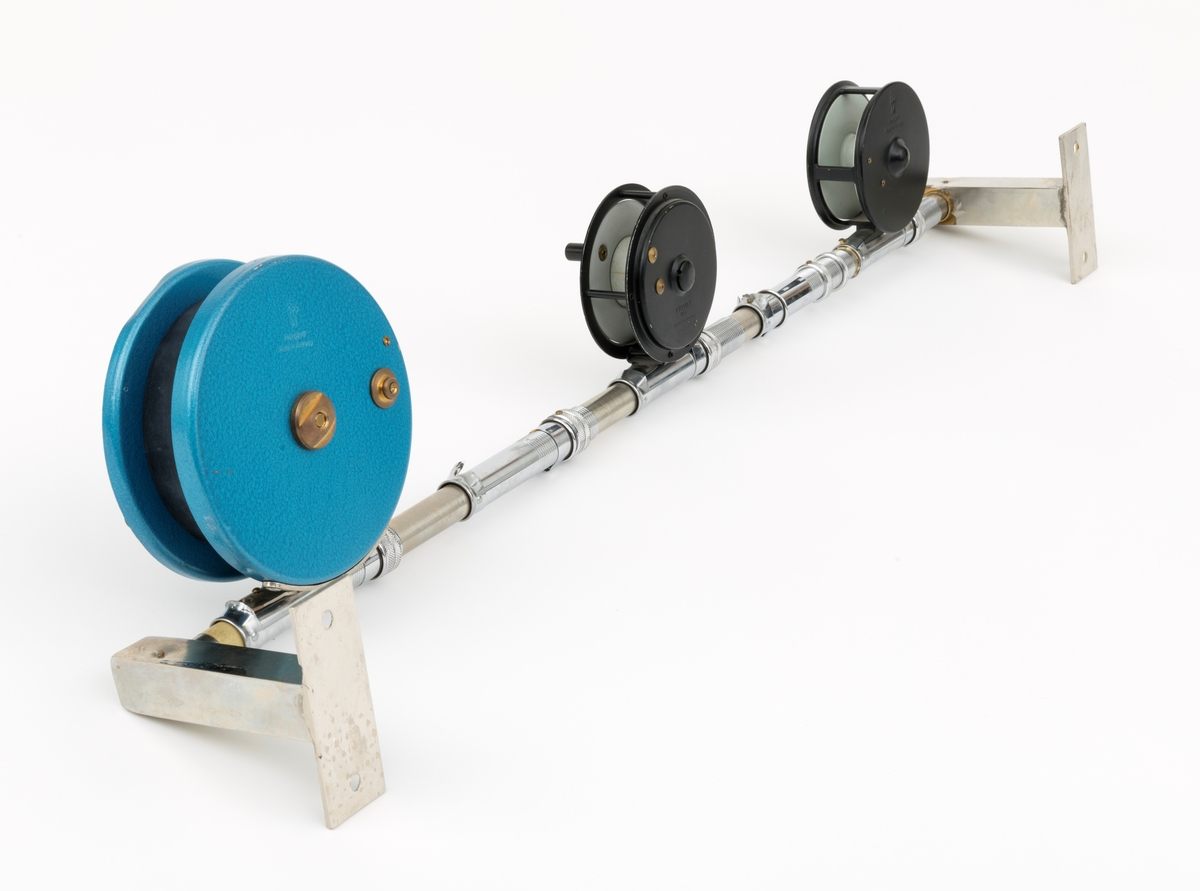 Tre fiskesneller, to fluesneller og en dorge- pilkesnelle, montert på et rør (en stang) med fem snellfester. I og med at det er fem snellefester kan det tyde på at det en gang har vært montert fem sneller på stanga. Snellene er produsert av firmaet Asbjørn Hørgård A/S i Trondheim. I hver ende av røret er det montert fester som gjør det mulig å montere stanga med fiskesneller til vegg. Snellene sitter festet på undersiden av stanga når de brukes, altså med snellefoten opp. 

I salgskatalogen "Råd og redskap fra Hørgård" i 1984 er den blå dorge- pilksnella  beskrevet slik: "Napptun snelle 51/2' * K(EK) Enklere kan en snelle knapt bli. Du kan enten bruke den som pilkesnelle eller du kan dorge med den på sjøen eller etter større innlandsfisk. Snelle har klikk som gir deg et signal når fisken går på. Klikken slår du på ved å skyve på knotten bak. Den store trommelen gjør at det er lett å ta inn fisk. På kanten av spolen har du en bremseflate, som du legger håndflaten på når fiske renner ut. Kan anbefales sammen Frøya. Pris: Napptun m/klikk kr. 205."
Diameter sidedeksel: 14 cm. Bredde målt frfa ytterside av sveivknapper til ytterside av sidedeksel: 8, 2 cm. 

Fluesnellene: Snellene består av spole (trommel), sidedeksler, ramme, sveiv og snellefot. Sveiva er montert direkte på spolen. 
På svart og hvit fluesnelle som er merket Trout Fly sitter sveivknappen løst. Snella merket Trout Fly har disse målene: 
Bredde målt fra ytterside av sveivknapp til ytterside av sidedeksel: 5,6 cm. Bredde spole, innvendig målt: 2,4 cm Diameter sidededeksel: 9,1 cm.
I Hørgård-firmaets bok "Norwegian made fishing tackle" fra 1964 er denne snelletypen beskrevet slik: "Trout Fly 3 1/2" Guttsnelle, passende for flue-, mark- og dorgefiske."

På svart og hvit fluesenlle som er merket Å H Hørgård er disse målene tatt: 
Bredde målt fra ytterside av sveivknapp til ytterside av sidedeksel: 6,4 cm. Bredde spole, innvendig målt: 2,2 cm Diameter sidededeksel: 8,9 cm.
I Hørgård-firmaets bok "Norwegian made fishing tackle" fra 1964 er denne snelletypen beskrevet slik: "Ørret fluesnelle 3 1/2'' ca. 170 gr. Presjonsarbeid med utsøkt materiale. Helstøpt lettmetall. Brennlakkert. Kapasitet: 30 yds. tapered fluesnøre og ca. 50 yds. bakline."



[Se fanen Opplysninger for informasjon om Asbjørn Hørgård og hans firma.]