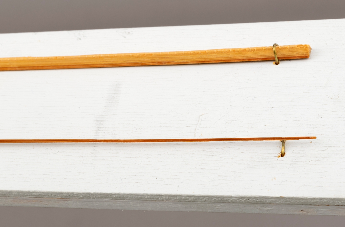 To splitcaneribber, spildrer av bambus (tonkinbambus), montert på en hvitmalt treplate. Spildrene har sitt utgansgpunkt i et bambusråemne (tonkinbambus) som er splittet opp og industrielt behandlet i firmaet Asbjørn Hørgårds maskiner, for deretter å bli limt sammen til fiskestenger.  Montasjen med de to spildrene har vært utstilt i museets basisutstilling om ferskvannsfiske fram til cirka 2013.

På den hvite treplata ses øverst en 1. gangs høvlet spildre før 2. gangs høvling og nederst en spildre (ribbe) etter 2. gangs høvling og som regnes som ferdig høvlet. En stangdel i ferdige fiskestanga, splitcanestanga, bestod av 6 ribber (spildrer). 

[Se referanser og referanser til filer for mer informasjon om hvordan framstillingen av splitkeinstenger foregikk. Se fanen "Opplysninger" for informasjon om Asbjørn Hørgård og hans firma. ]