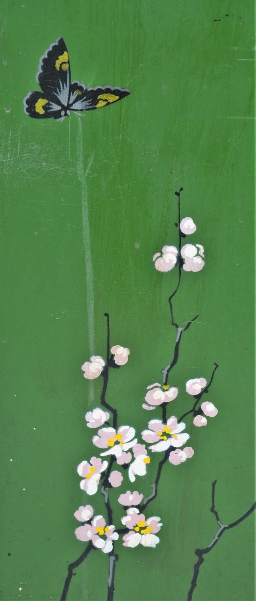 Svart skjermbrett av metall bestående av tre rektangulære paneler som hver står på to føtter. Panelene er dekorert med påmalt dekor i form av grønt vindu med grener med hvite blomster, samt sommerfugl og fugl, innrammet av tre tynne, gullborder.