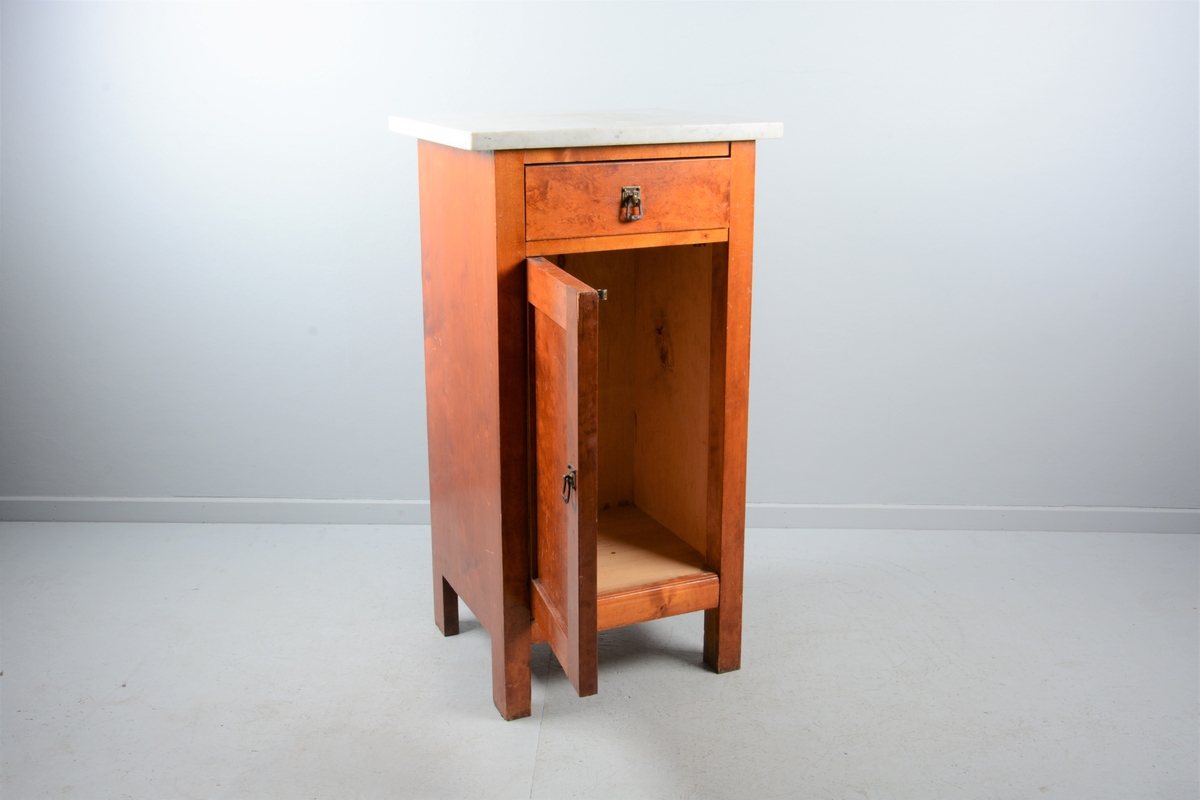 Nattbord med skuff, skap og marmorplate på toppen (plata er laus). Skuffen og skapet har messingknotter. Skapet har fyllingsdør som har opning mot venstre og skal dermed stå på venstre side av senga.