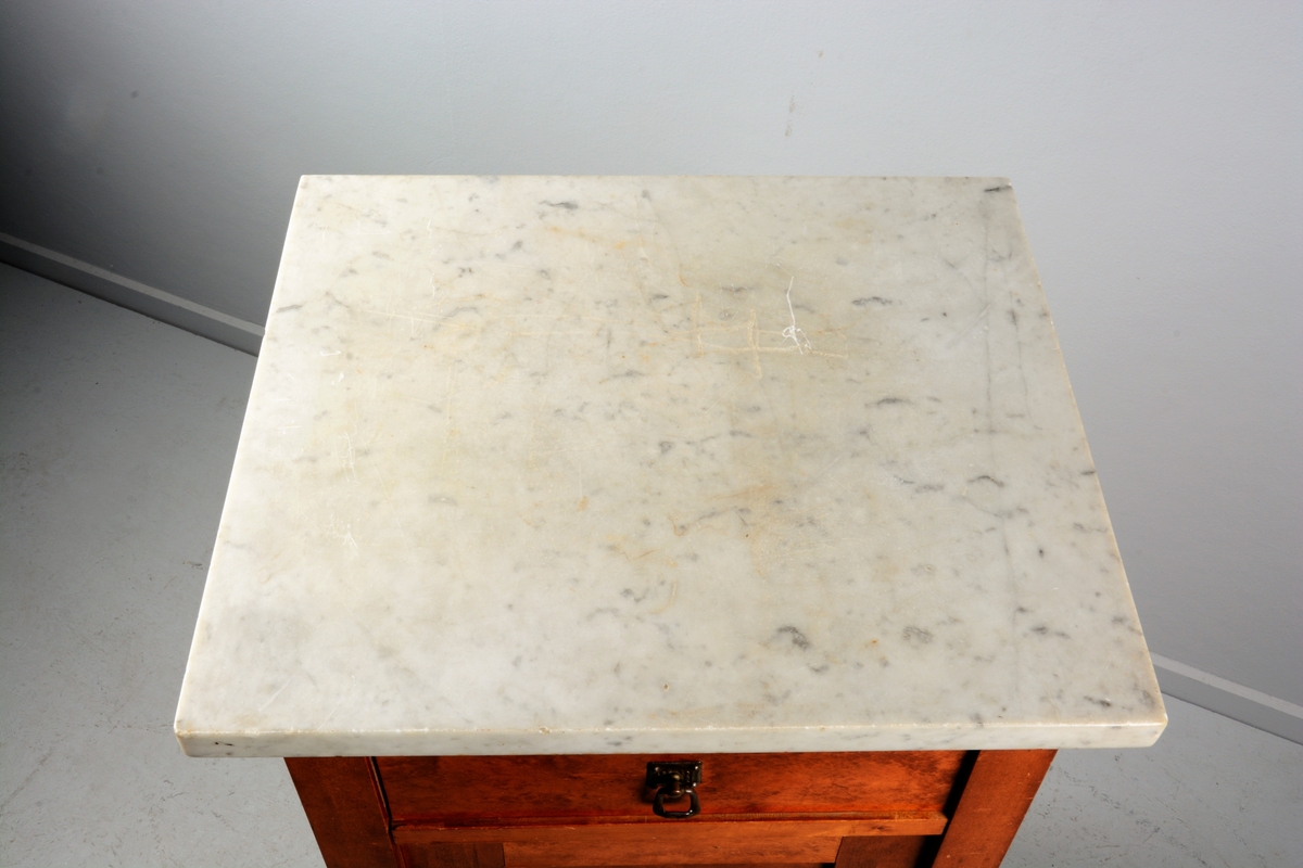 Nattbord med skuff, skap og marmorplate på toppen (plata er laus). Skuffen og skapet har messingknotter. Skapet har fyllingsdør som har opning mot venstre og skal dermed stå på venstre side av senga.