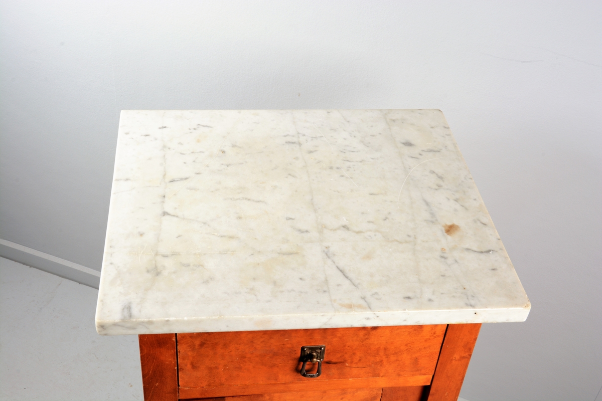 Nattbord med skuff, skap og marmorplate på toppen (plata er laus). Skuffen og skapet har messingknotter. Skapet har fyllingsdør som har opning mot venstre og skal dermed stå på venstre side av senga.
