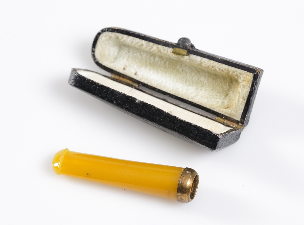 Cigarettmunstycke i bärnsten, nedre delen försedd med gul metallring. Tillhörande fodral i svart papp, inuti sammet och siden i gul färg.

Inskrivet i huvudkatalogen 1971.