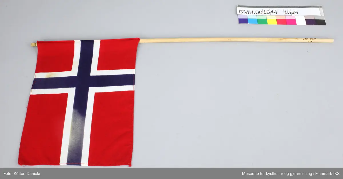 Ni norske flagg av eldre dato. Flaggene er av vevd bomullsstoff og omtrent like store. Pinnene er ulik lange, noen er knekt eller saget av, men alle har en kule, opprinnelig med gull maling på toppen.