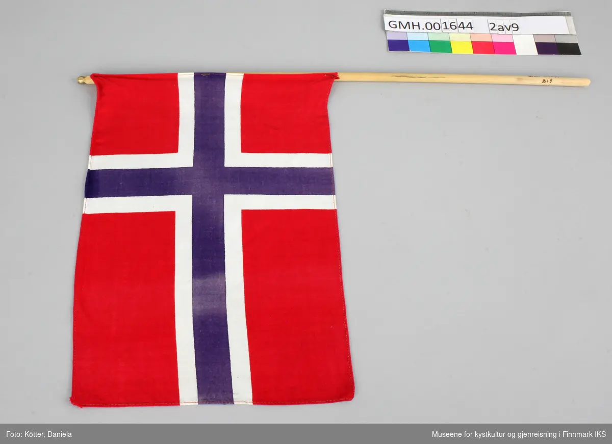 Ni norske flagg av eldre dato. Flaggene er av vevd bomullsstoff og omtrent like store. Pinnene er ulik lange, noen er knekt eller saget av, men alle har en kule, opprinnelig med gull maling på toppen.