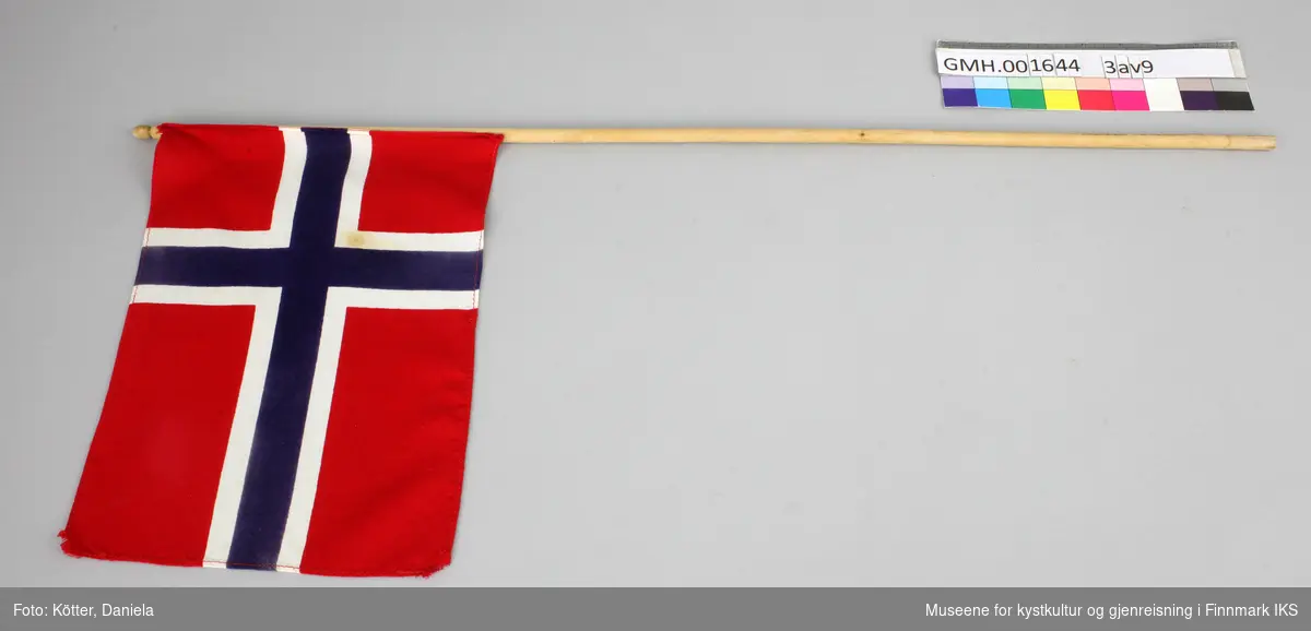 Ni norske flagg av eldre dato. Flaggene er av vevd bomullsstoff og omtrent like store. Pinnene er ulik lange, noen er knekt eller saget av, men alle har en kule, opprinnelig med gull maling på toppen.