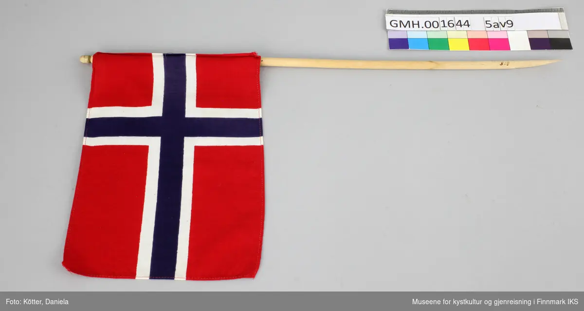 Ni norske flagg av eldre dato. Flaggene er av vevd bomullsstoff og omtrent like store. Pinnene er ulik lange, noen er knekt eller saget av, men alle har en kule, opprinnelig med gull maling på toppen.
