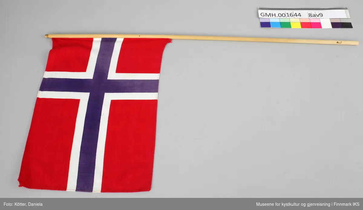 Ni norske flagg av eldre dato. Flaggene er av vevd bomullsstoff og omtrent like store. Pinnene er ulik lange, noen er knekt eller saget av, men alle har en kule, opprinnelig med gull maling på toppen.