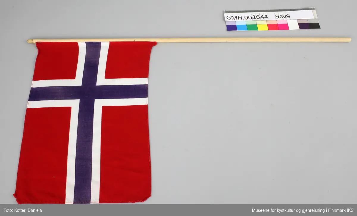 Ni norske flagg av eldre dato. Flaggene er av vevd bomullsstoff og omtrent like store. Pinnene er ulik lange, noen er knekt eller saget av, men alle har en kule, opprinnelig med gull maling på toppen.