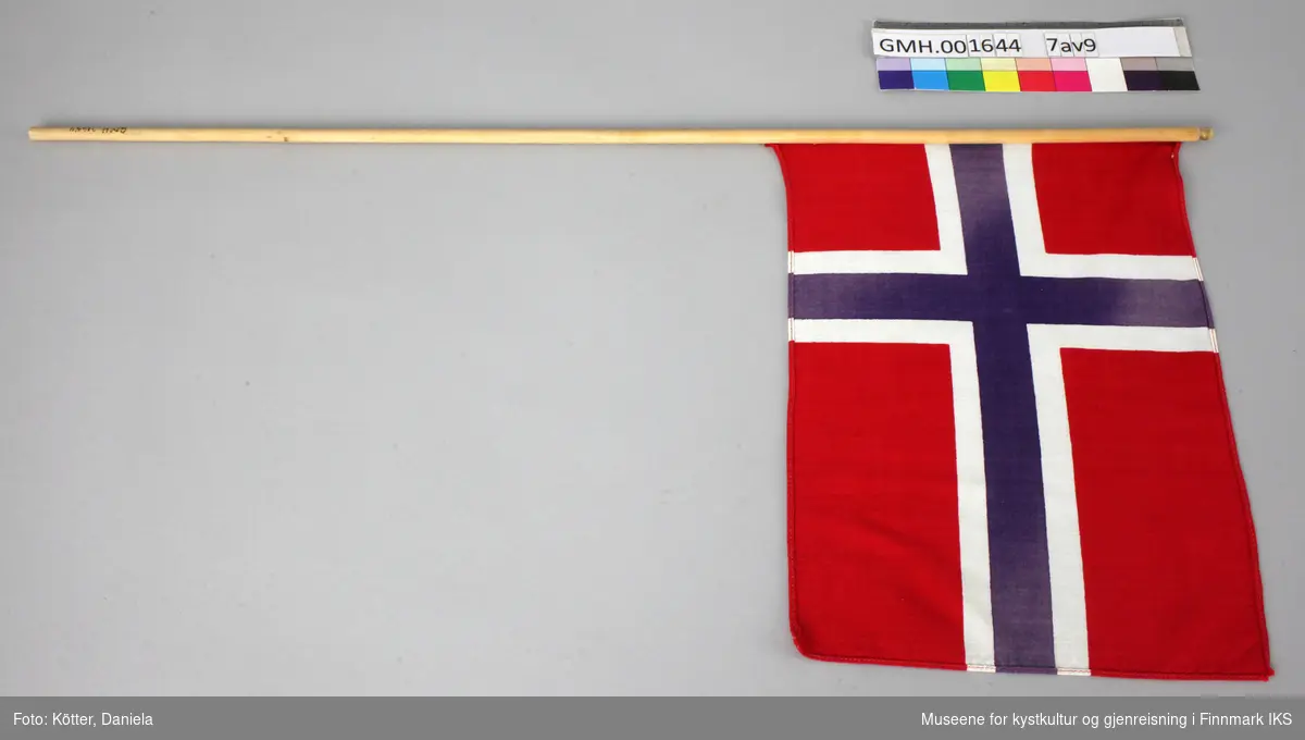 Ni norske flagg av eldre dato. Flaggene er av vevd bomullsstoff og omtrent like store. Pinnene er ulik lange, noen er knekt eller saget av, men alle har en kule, opprinnelig med gull maling på toppen.