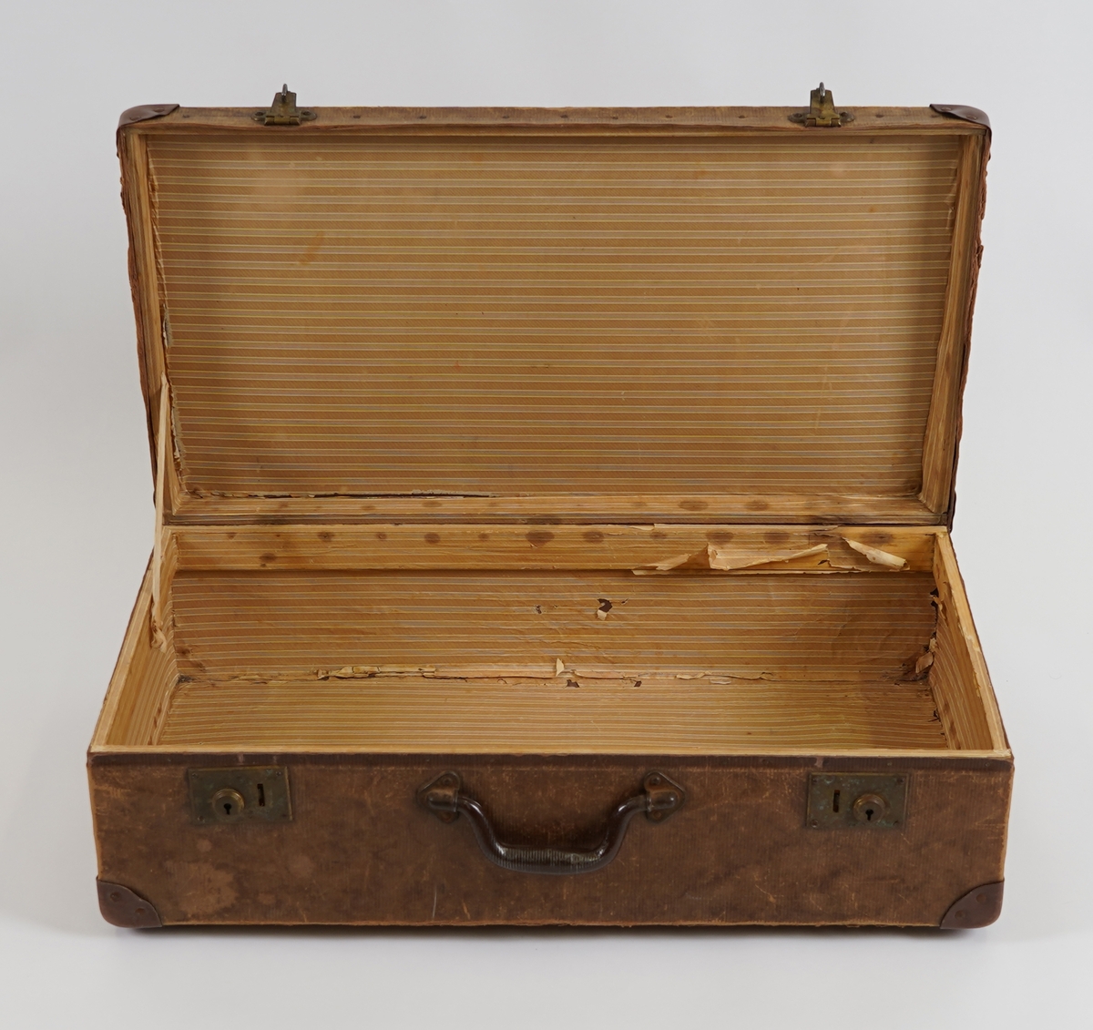 Ein rektangulær koffert, laga av pappliknande materiale, på ei innvendig treramme. Hjørna er forsterka med skinn. Handtak, henglser og låsar er i metall.