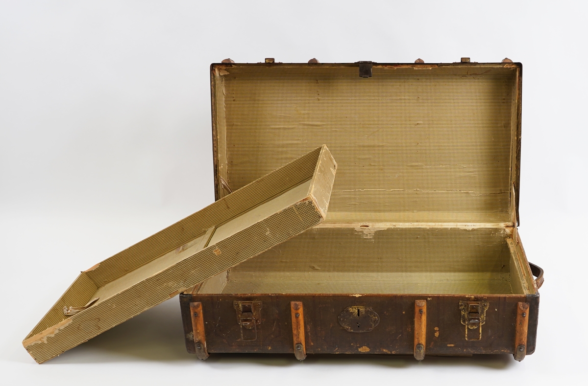 Koffert av tre kledd med strie på utsida og papir på innsida. På utsida er det beslag av tre forsterka med metall. Innvendig er kofferten delt med ei skuff til å løfte opp.