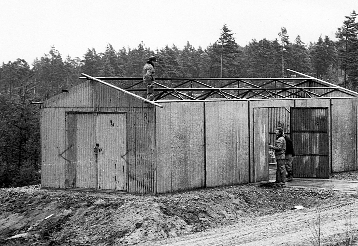 Nybyggnation av tre förråd 1986.

Utöver det tre förråden vid lägret monterades också ett enkelt emballageförråd vid ammunitionsförrådet på ön. Plåtskjulet hade tidigare stått vid Miloverkstaden i Strängnäs.

Denna typ av skjul byggdes också i vallbydalgången på Härads skjutfält och vid ammunitionsförrådet på N fältet i Strängnäs (typ E VI u).

Bild 1: Kurt Madell på taket och Kjell Strömkvist i dörröppningen.

Bild 2: Kurt på taket och hantverkaren Einar Lantz.

Bild 3: Einar ser ut att hålla på med någon metalltråd.

Bild 4: Hantverkaren Lars-Olov Sellberg mäter upp takplåt.

Bild 5: Kjell Strömkvist skruvar ihop väggsektioner.