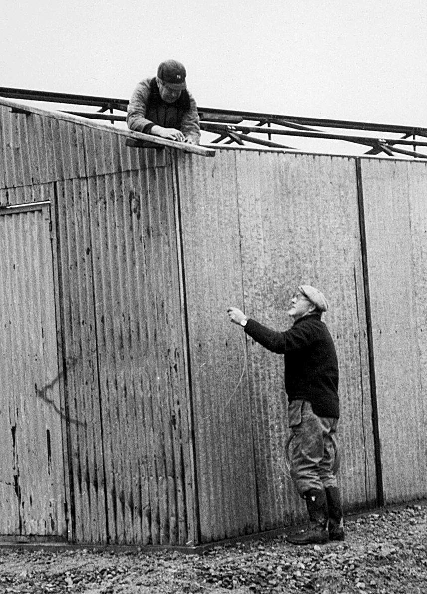 Nybyggnation av tre förråd 1986.

Utöver det tre förråden vid lägret monterades också ett enkelt emballageförråd vid ammunitionsförrådet på ön. Plåtskjulet hade tidigare stått vid Miloverkstaden i Strängnäs.

Denna typ av skjul byggdes också i vallbydalgången på Härads skjutfält och vid ammunitionsförrådet på N fältet i Strängnäs (typ E VI u).

Bild 1: Kurt Madell på taket och Kjell Strömkvist i dörröppningen.

Bild 2: Kurt på taket och hantverkaren Einar Lantz.

Bild 3: Einar ser ut att hålla på med någon metalltråd.

Bild 4: Hantverkaren Lars-Olov Sellberg mäter upp takplåt.

Bild 5: Kjell Strömkvist skruvar ihop väggsektioner.